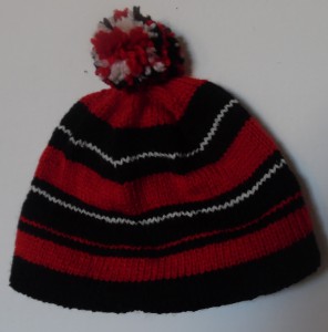 Tophue strikket i røde, hvide og sorte striber med pompom i de samme farver